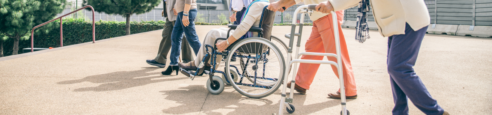 People using medical equipment rental including a wheelchair and a walk while out in an open area with concrete and steps