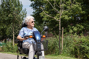 Elderly woman using electric scooter outside on a paved path