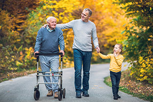 Elderly man using walking aid outside on paved path while walking with son and grandson
