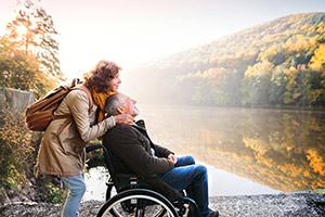 Man sitting in wheelchair with wife standing behind him looking out over river and trees